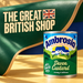 Ambrosia Devon Custard 400g tin beneath a sculptural emerald painted birch curve with integral ivory Great British Shop branding and a custard-gold ground.